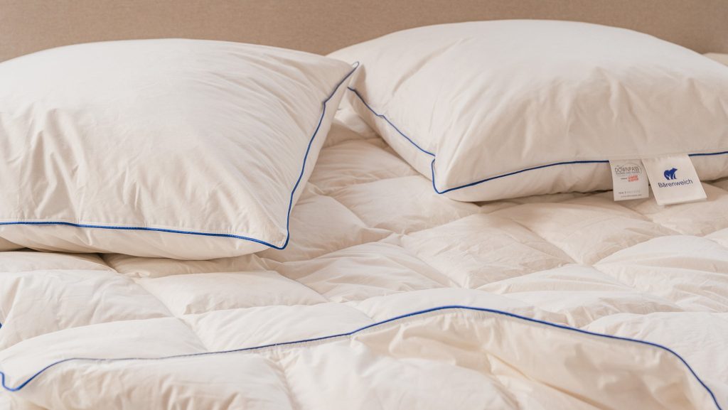 Bruno Bärenweich Kissen und Bettdecke mit blauer Paspel auf einem Bett