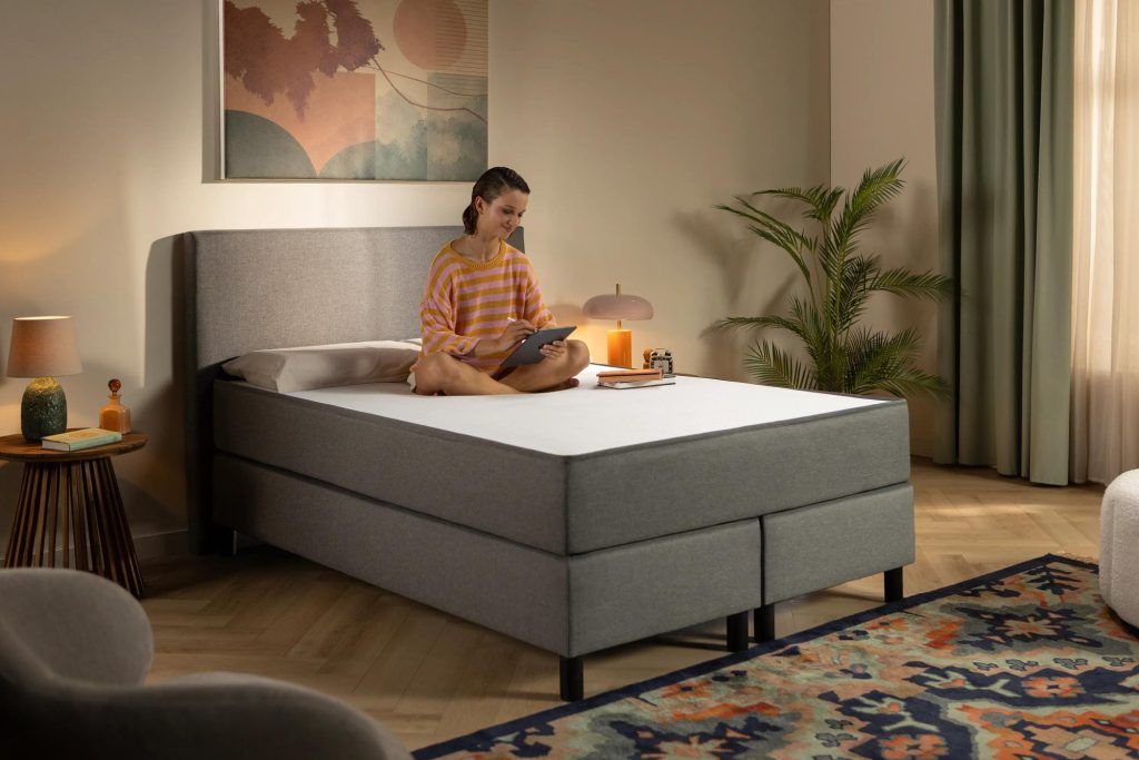 Frau sitzt mit Tablet auf dem Emma Original Boxspringbett Komfort
