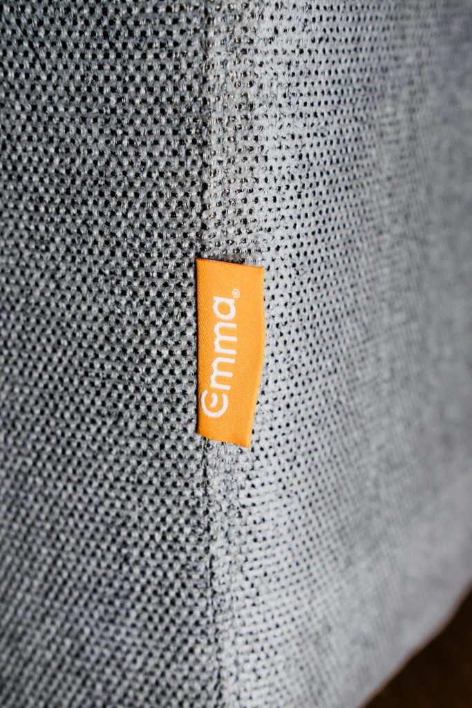 Grauer Webstoff des Emma Original Schlafsofas mit orangefarbenem Emma-Etikett