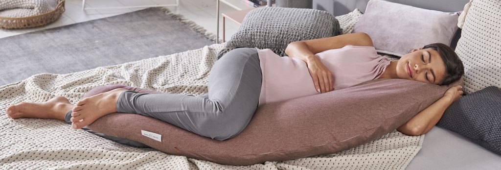 Schwangere liegt auf der Seite und stützt Bauch und Kopf mit dem Theraline Das Original Stillkissen