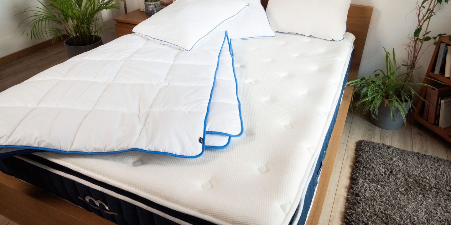 Matratze mit Bettdecke und zwei Kopfkissen auf einem Holzbett in einem hellen Schlafzimmer
