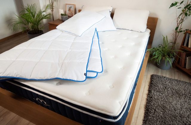 Matratze mit Bettdecke und zwei Kopfkissen auf einem Holzbett in einem hellen Schlafzimmer