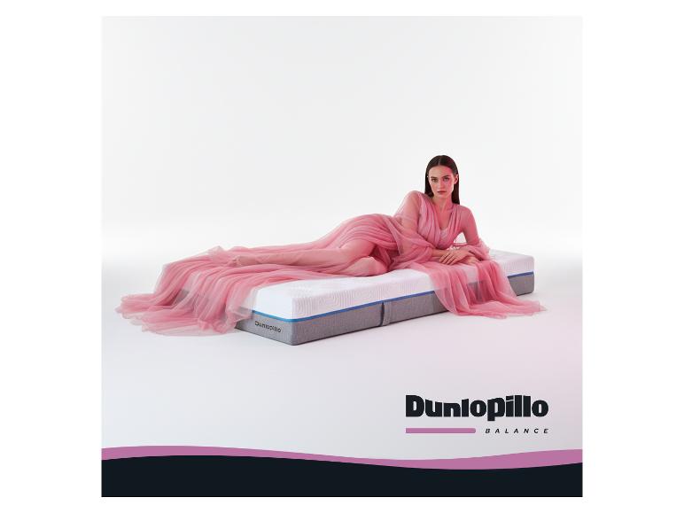 Frau in rosa Kleid sitzt auf der Dunlopillo Balance T Matratze