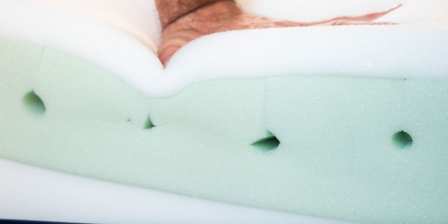 Hand drückt in freigelegte Schaumschichten einer Matratze