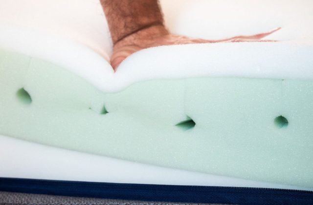 Hand drückt in freigelegte Schaumschichten einer Matratze