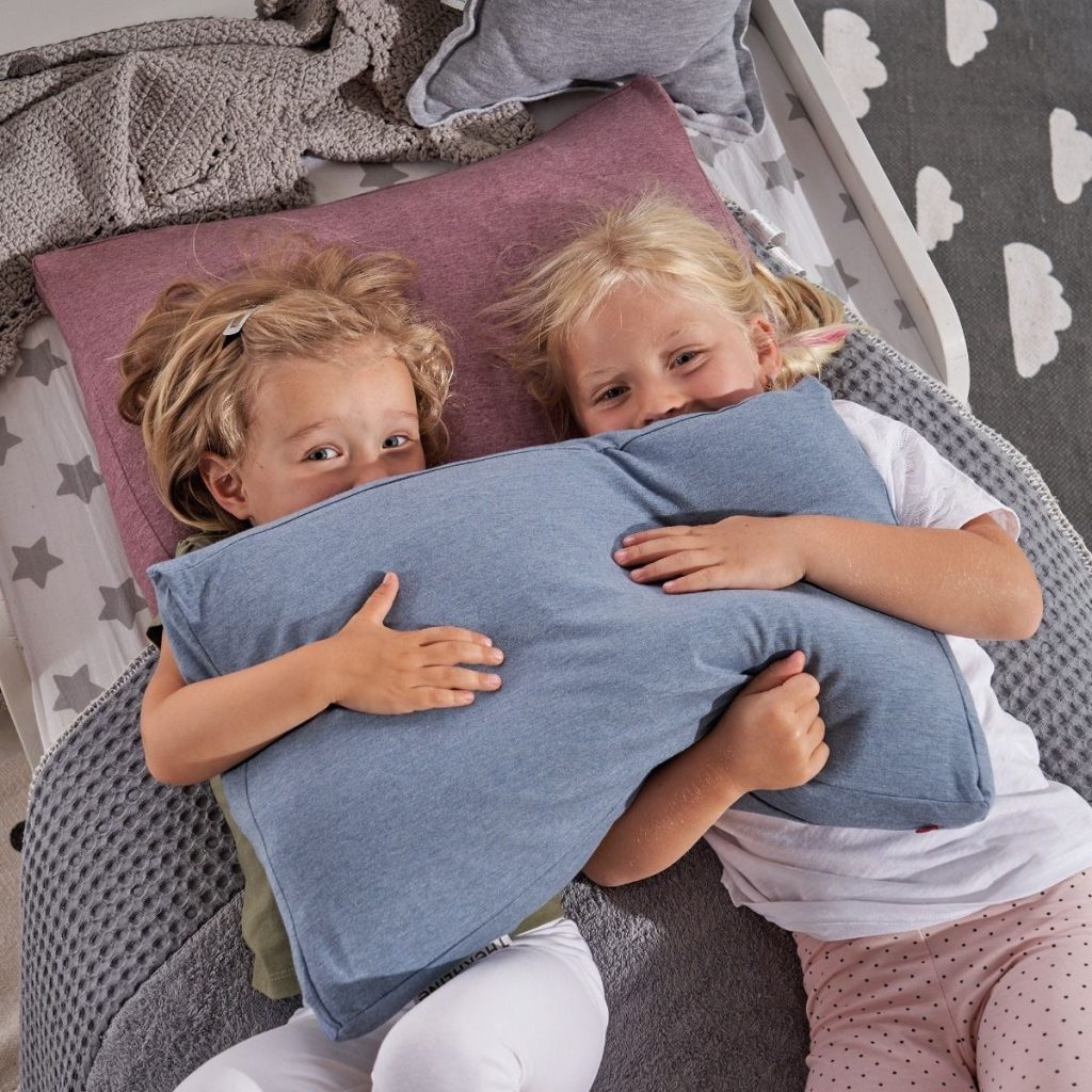 Zwei Kinder umarmen das Theraline Kinderkopfkissen im Bett