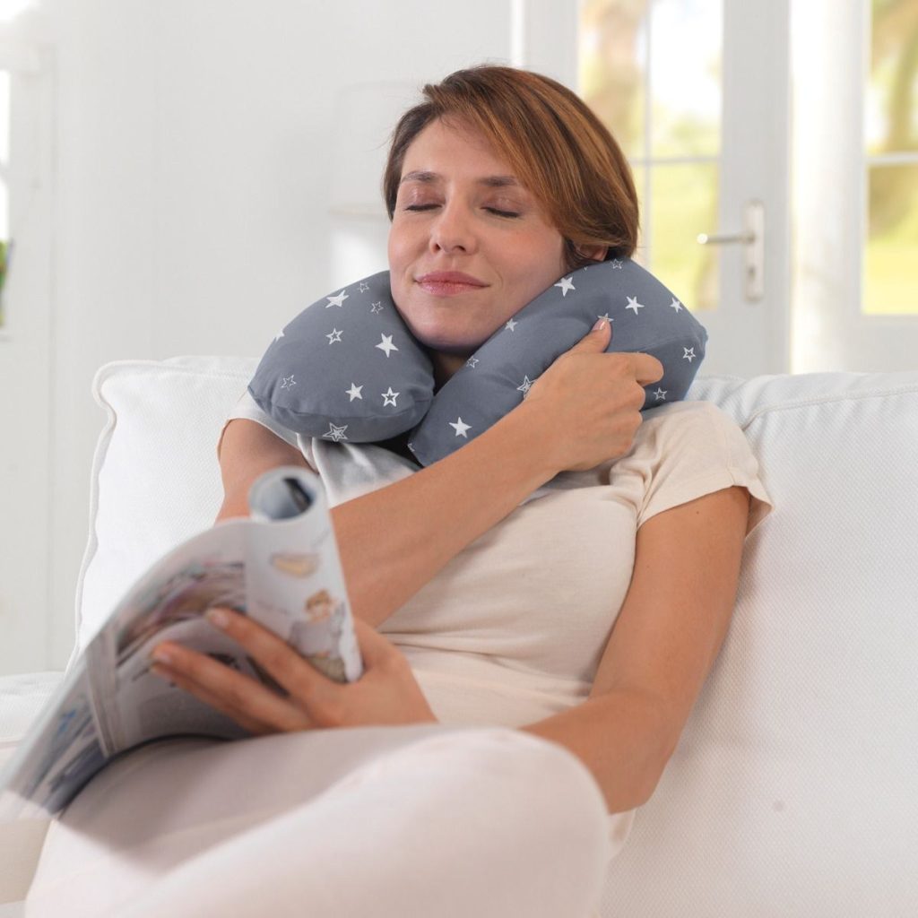 Frau mit dem Theraline Schlaf- und Nackenkissen um den Nacken auf dem Sofa