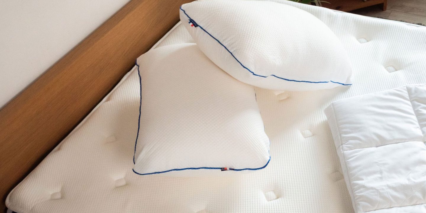 Zwei weiße Kopfkissen mit blauer Paspel auf einer Matratze
