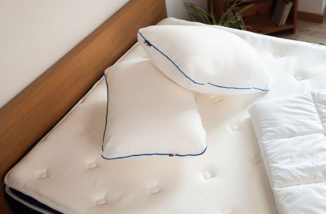 Zwei weiße Kopfkissen mit blauer Paspel auf einer Matratze